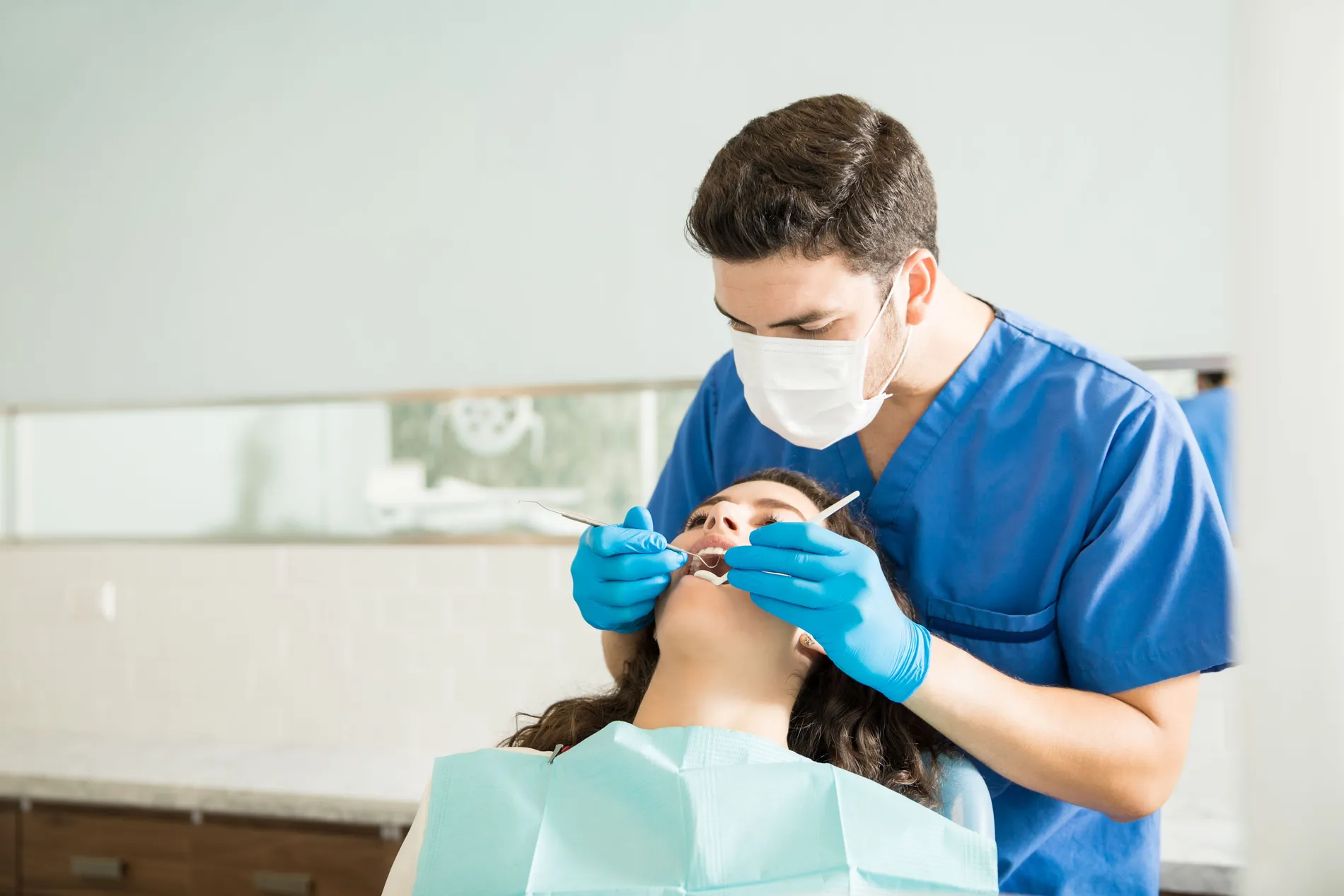 male_dentist_examining_young_woman_with_dental_carver_medical_clinic_a9a210dd02
